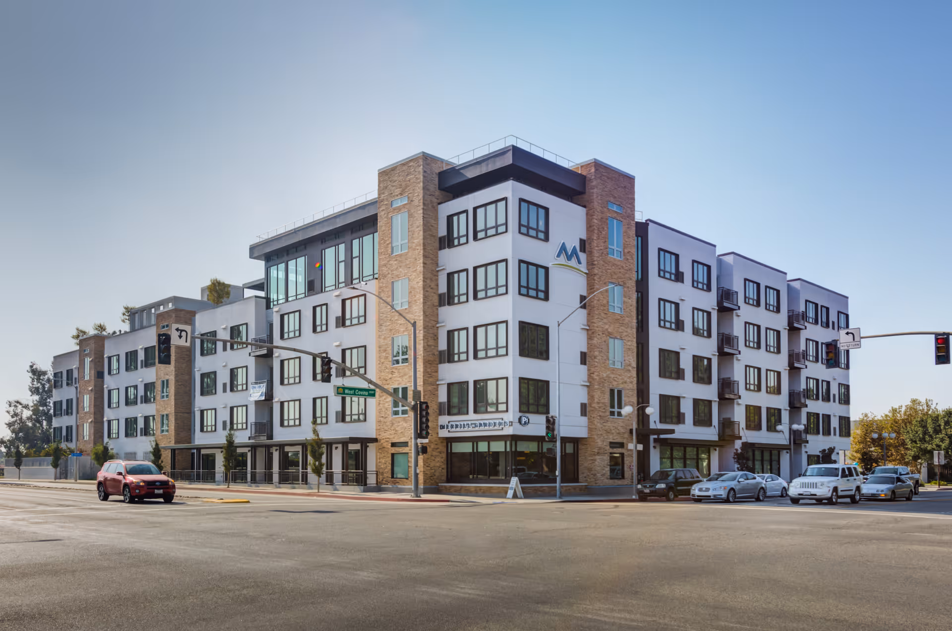 Modern five-story apartment-style senior living building on a street corner with cars parked along the curb.