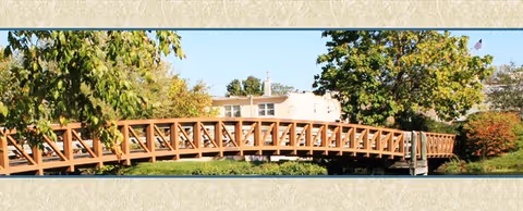 Wooden pedestrian bridge arches across a grassy area with trees surrounding a facility.