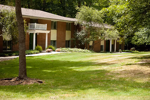 Exterior view of a two-story brick building surrounded by trees and greenery with a well-maintained lawn in front.