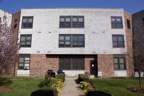 Front view of a three-story senior living building with white upper facade and brick base.