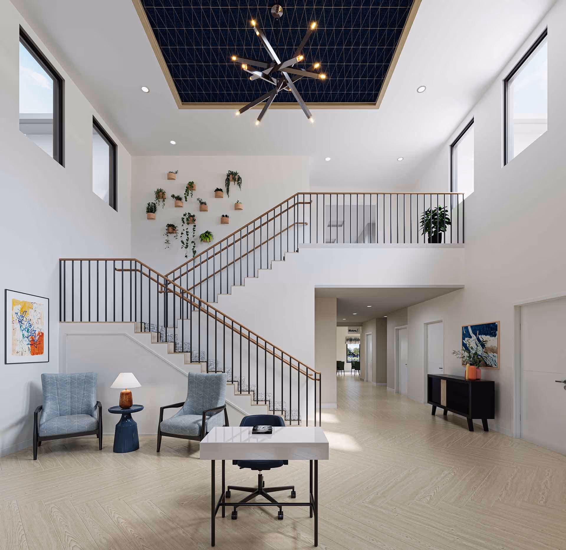 Bright and spacious interior of a senior living facility featuring a modern staircase with black railings and wooden handrails, two blue armchairs with a small table and lamp between them, a white desk with a black office chair, potted plants on the wall and on a ledge, abstract artwork on the walls, and a large geometric chandelier hanging from a recessed ceiling with a dark blue patterned inset.