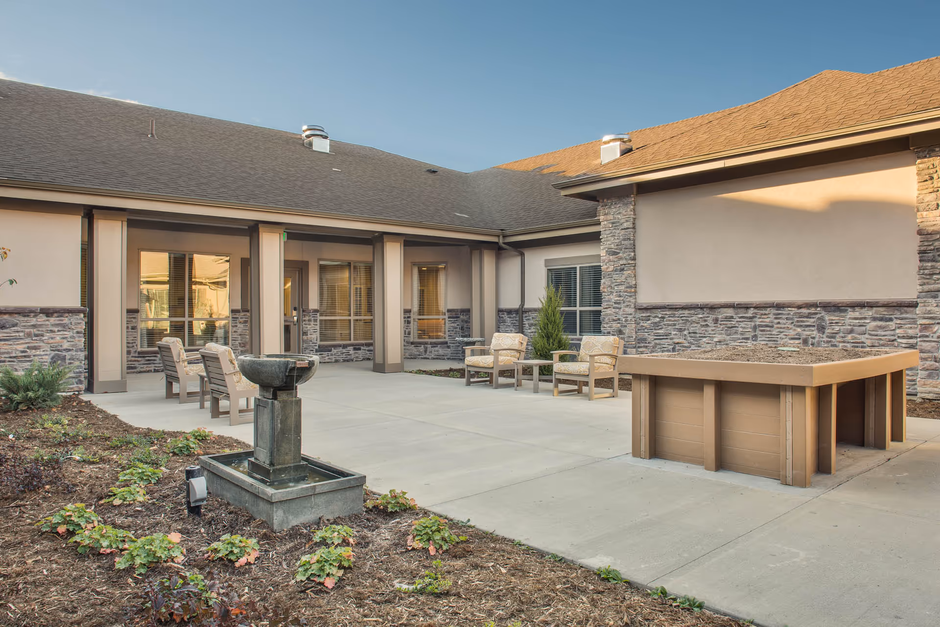 Outdoor courtyard with patio chairs, a small fountain, and a raised planter in front of a single-story building.