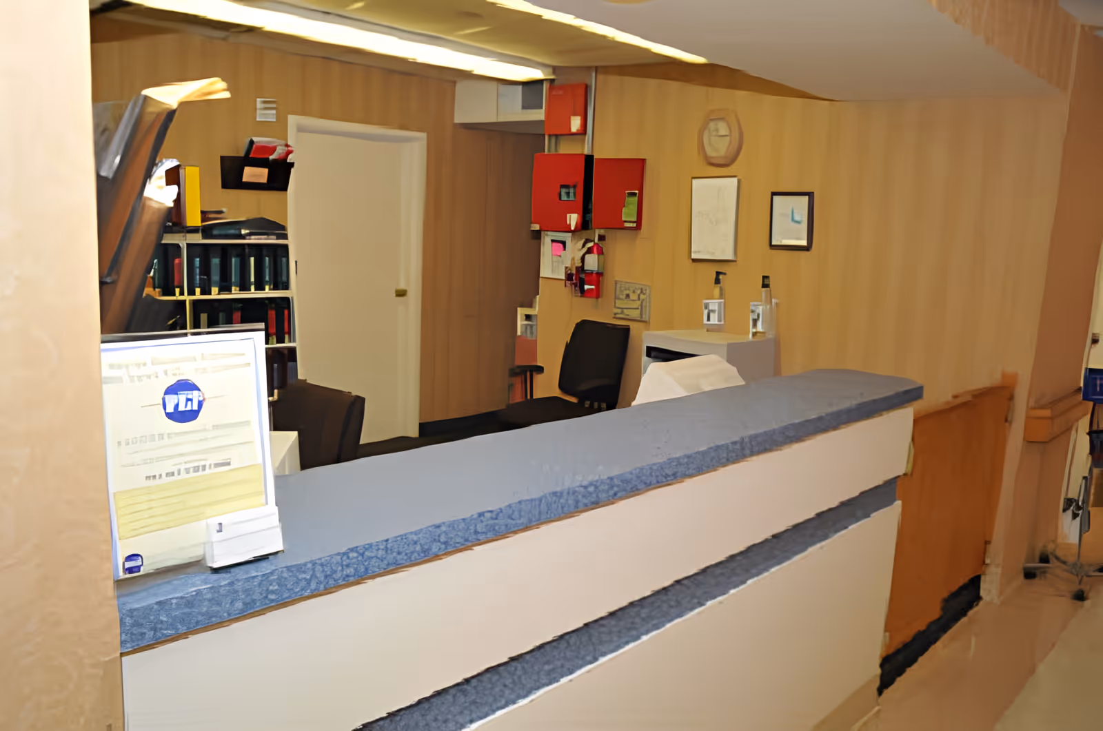 Reception desk area inside a senior living facility with a counter, computer monitor, chairs, and wall cabinets.