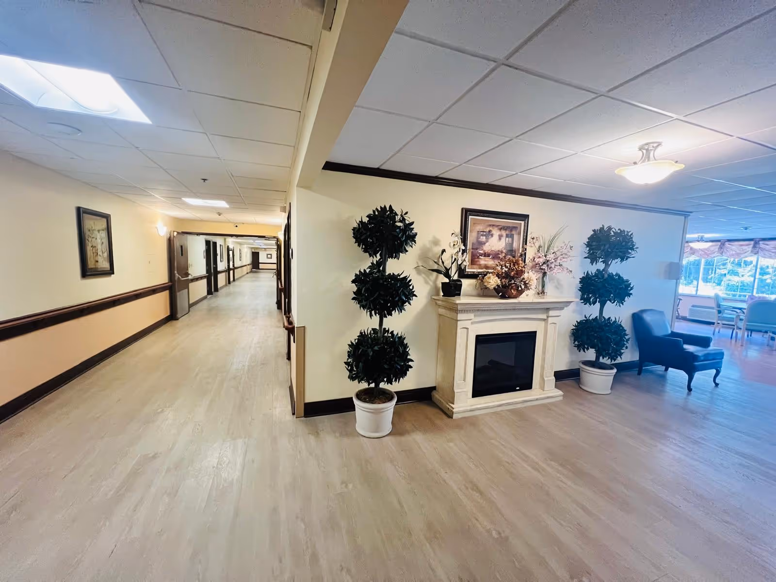 A hallway in a senior living facility featuring decorative plants and a fireplace.