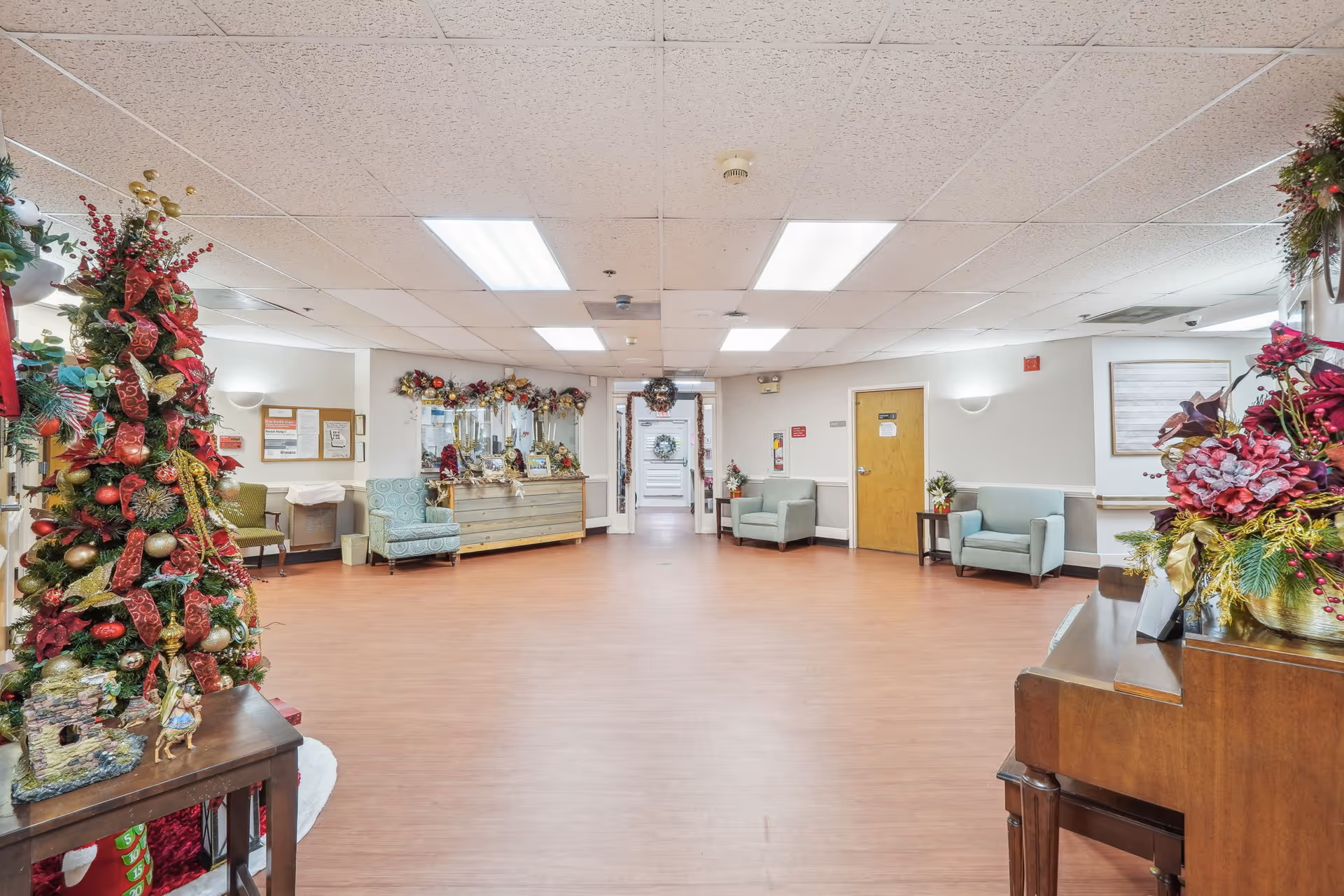 Spacious decorated lobby/common area in a senior living facility with holiday decorations, seating, and a reception desk.