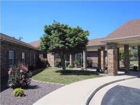 Brick building with a covered entrance, curved walkway, and a tree in landscaped front yard.