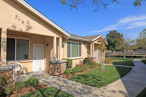 Exterior of Arbor Faire Senior Apartments with a walkway, shrubs, and a small seating area.
