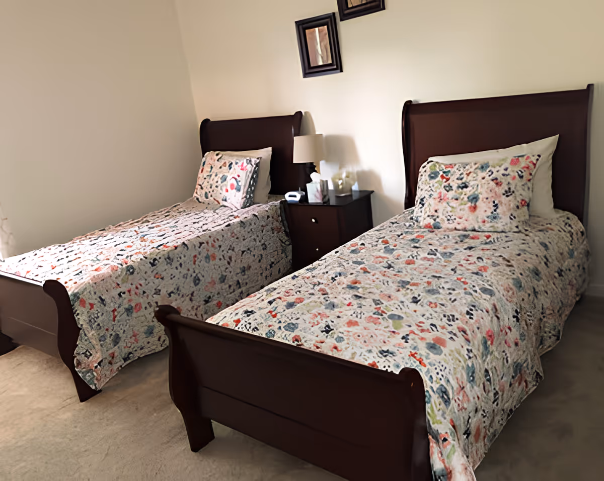 Two twin beds with floral bedspreads and a nightstand with a lamp in a bedroom.
