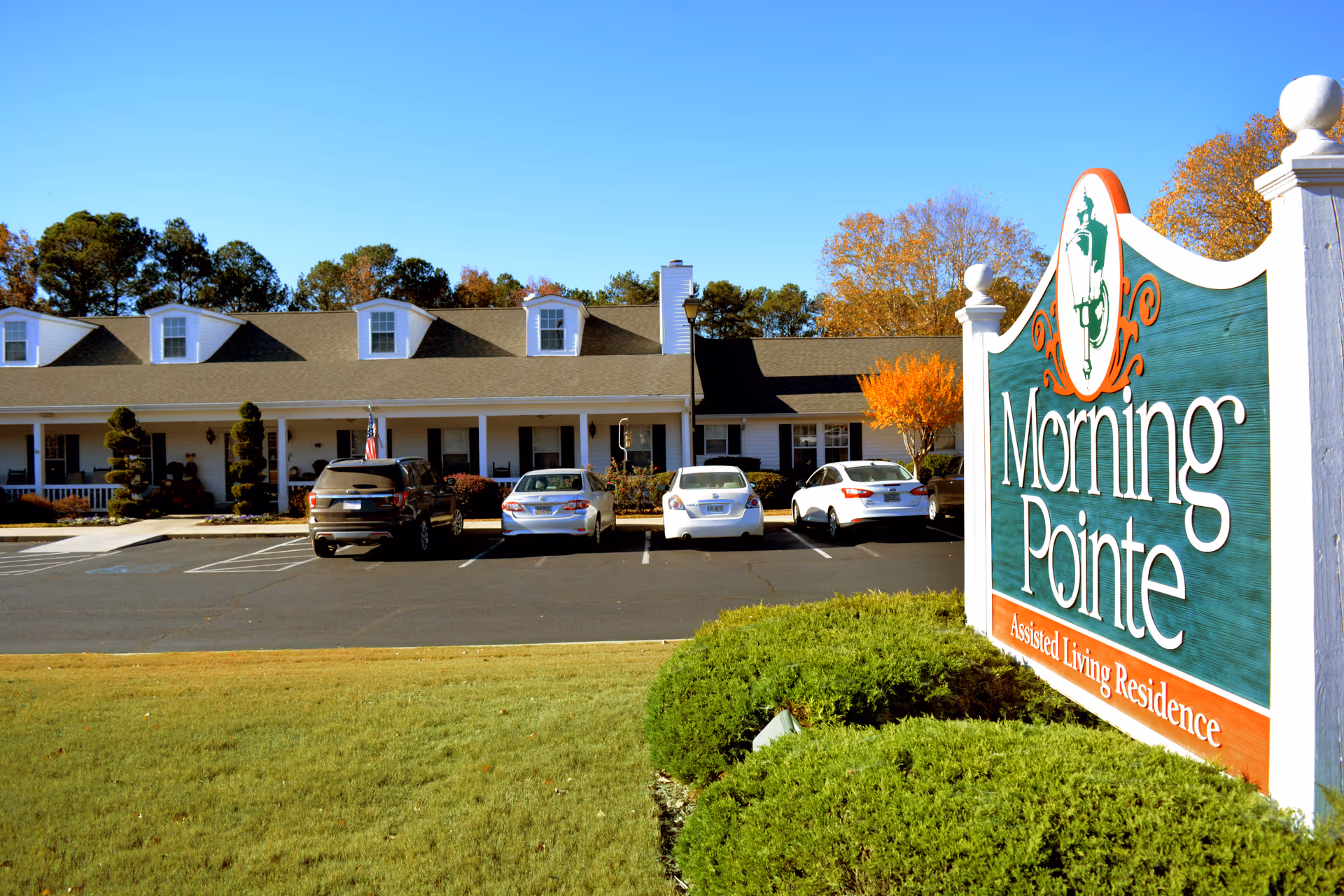 Front exterior of Morning Pointe assisted living with the facility sign in the foreground and parked cars.