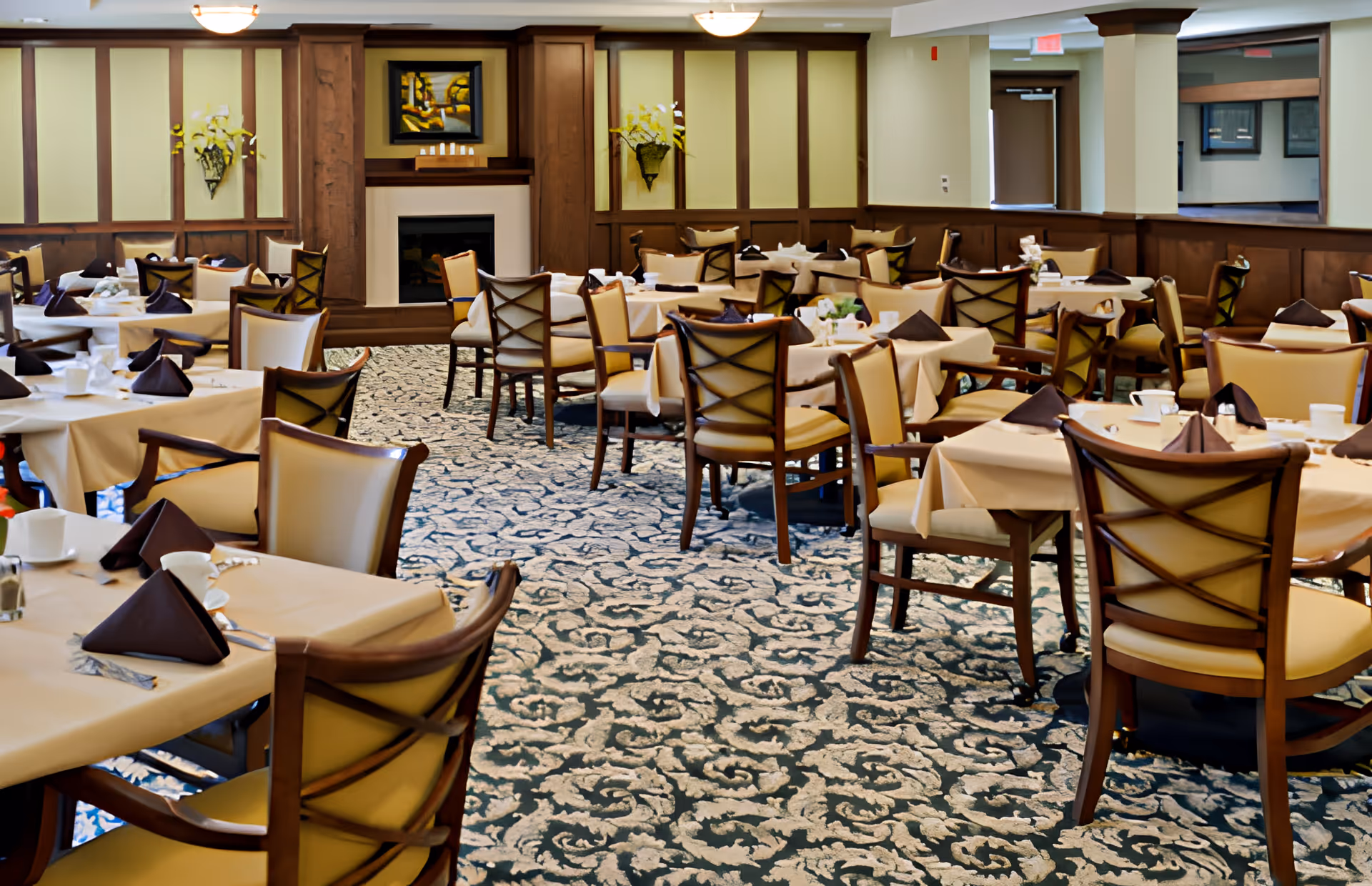 Spacious dining room with multiple set tables, upholstered chairs, and a fireplace.
