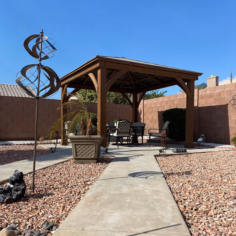 Wooden gazebo with seating under a covered patio in a fenced desert backyard.