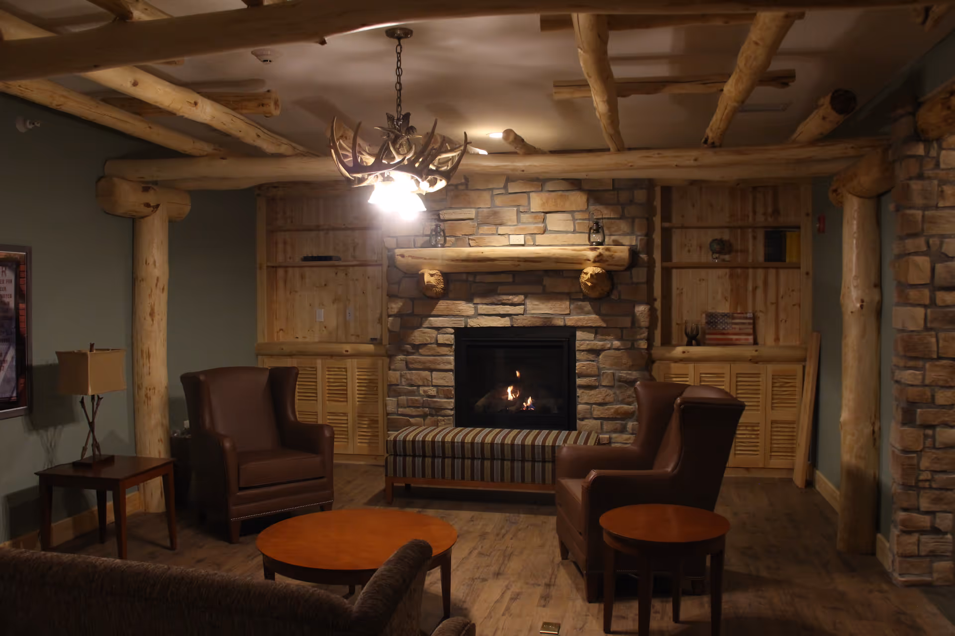 Cozy lodge-style lounge with a stone fireplace, exposed log beams, armchairs, and coffee tables.
