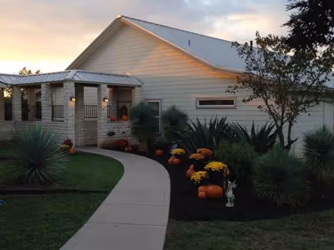 Front view of a light-colored assisted living facility with pumpkins along the walkway.