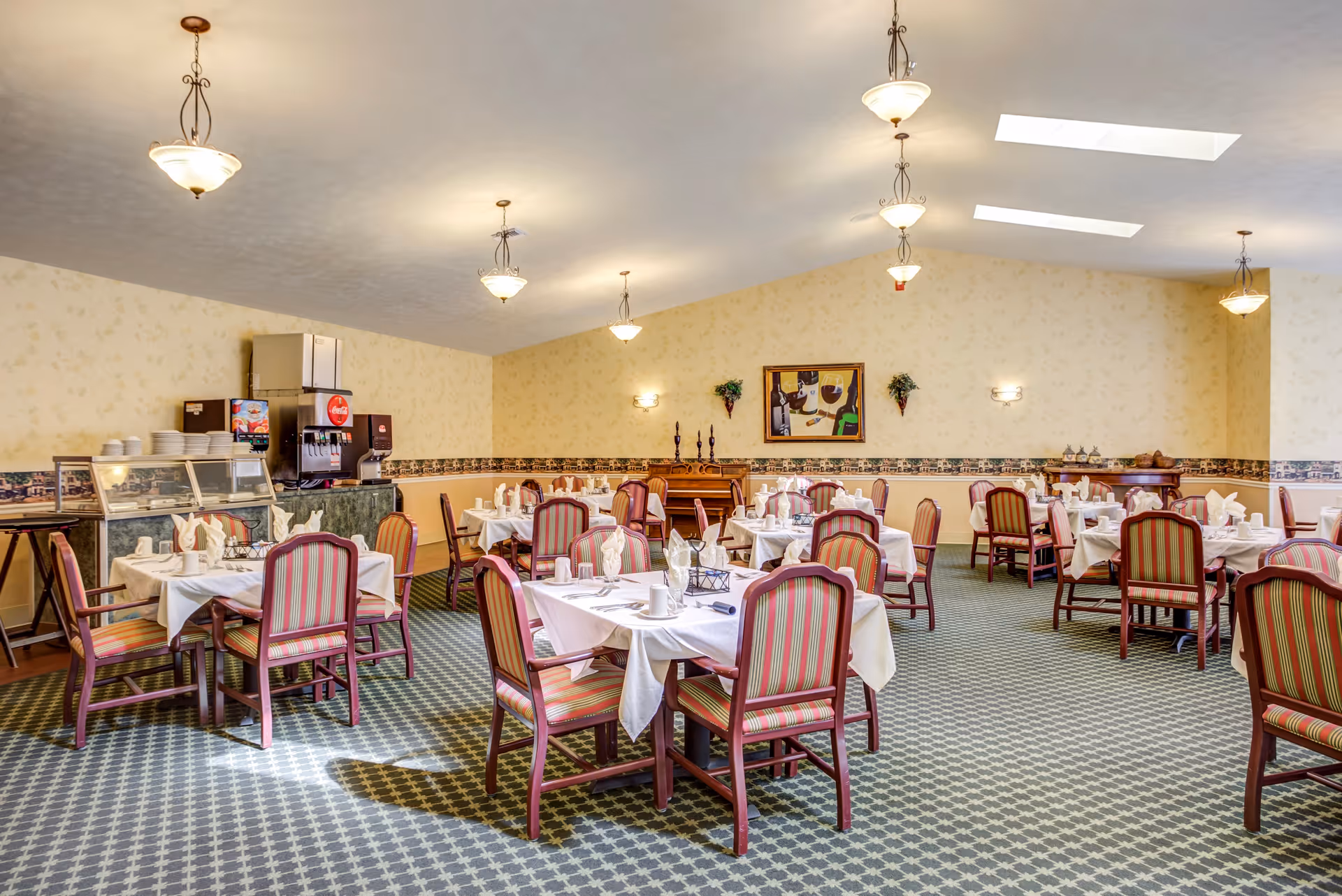 Spacious dining room with multiple set tables, striped chairs, and a beverage station under pendant lights.