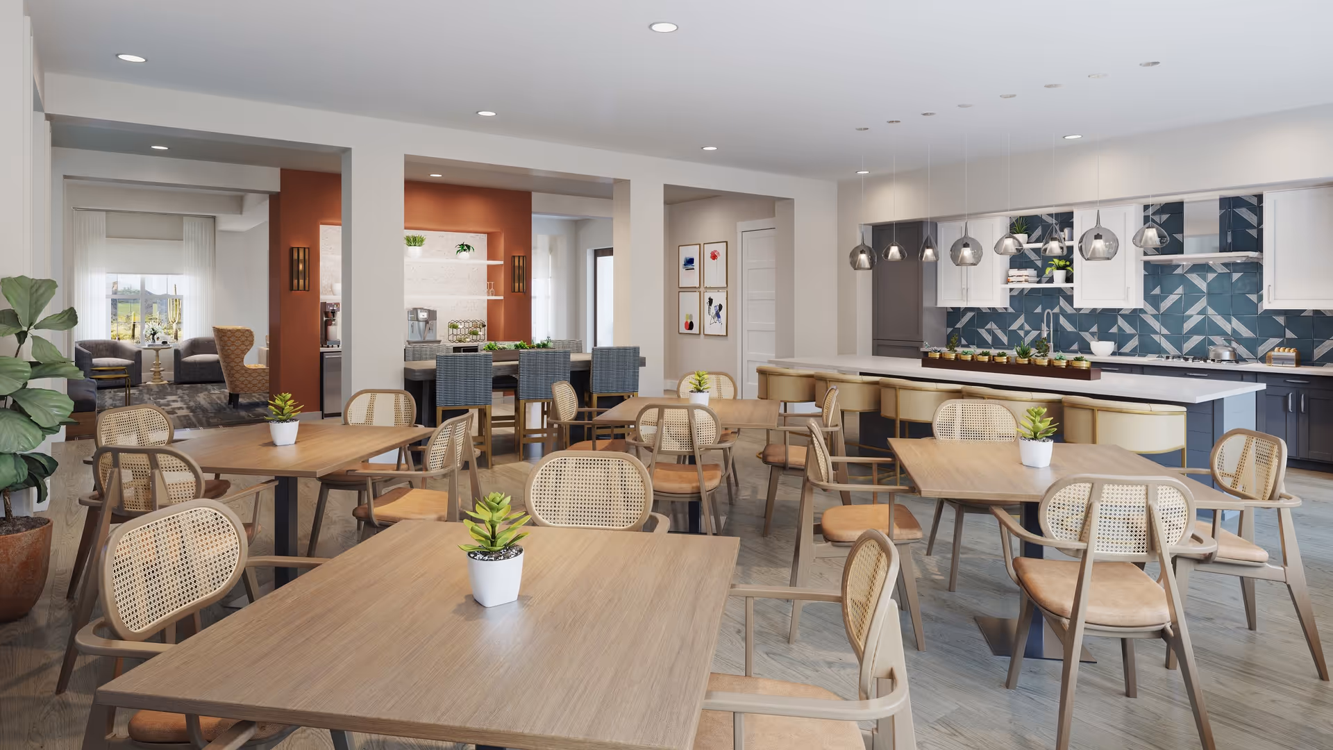 Bright communal dining area with multiple wooden tables and cane-back chairs, small potted plants, and a modern kitchen island in the background.
