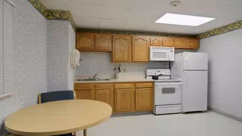Small kitchen with wooden cabinets, round table, and white appliances in a compact room.