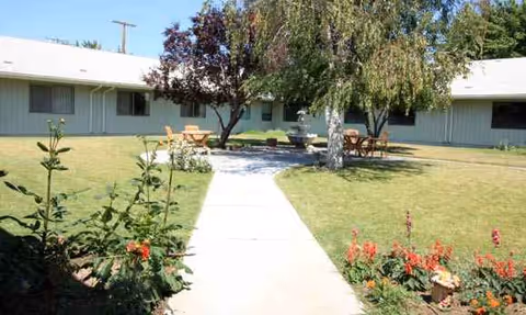 Single-story nursing home exterior with a central courtyard, trees, and outdoor seating.