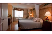 Shared residential bedroom with two twin beds, bedside tables and lamps, a dresser, and a window with a floral valance.