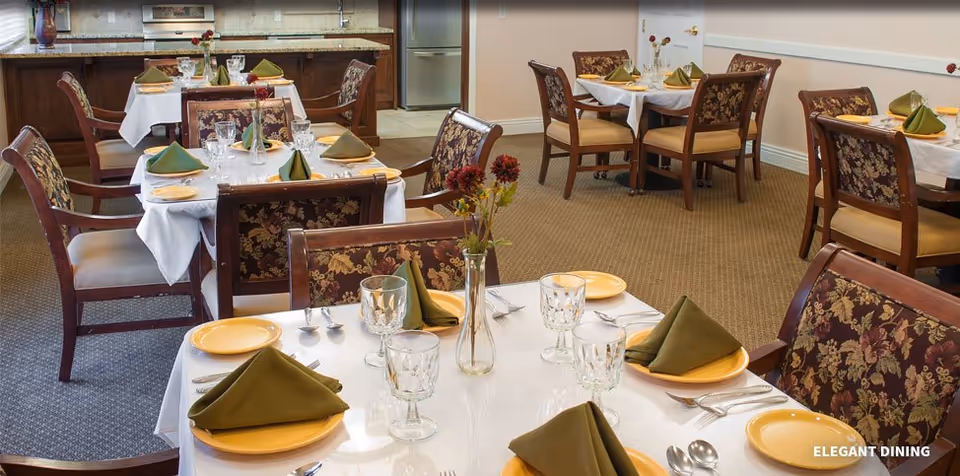 Dining room with multiple set tables, floral-upholstered chairs, white tablecloths and folded green napkins.