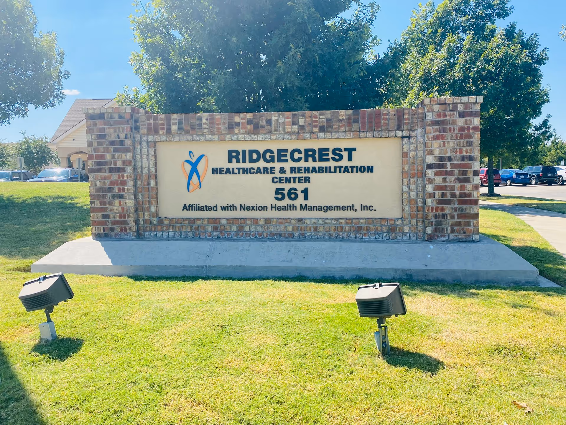 Brick monument sign on a grassy lawn that reads "Ridgecrest Healthcare & Rehabilitation Center 561" in front of the facility.