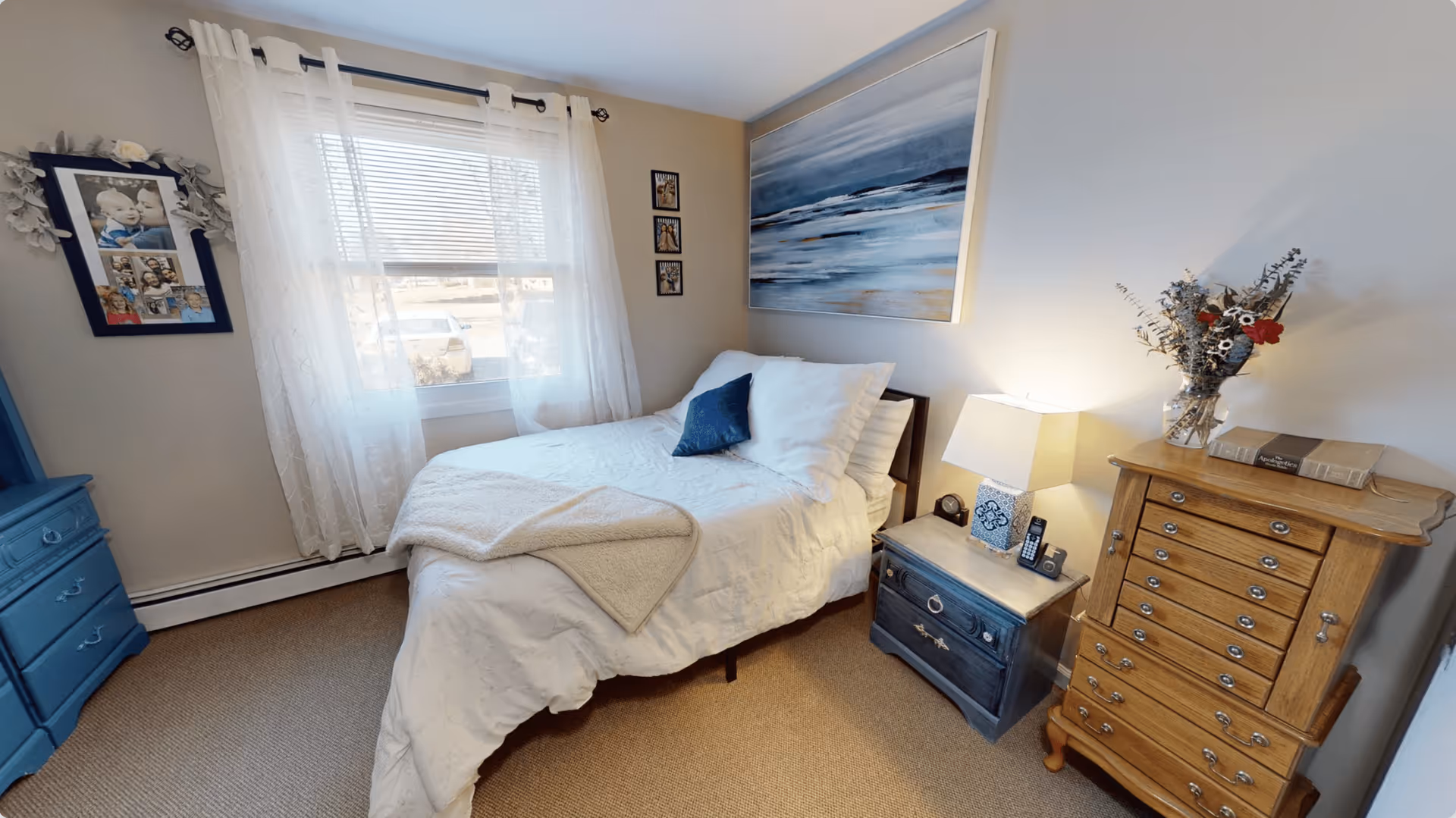 Cozy, well-decorated bedroom with a bed, nightstands, dressers and a window with sheer curtains.