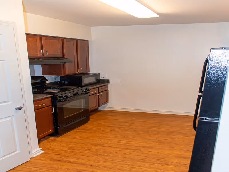 Kitchen with dark wood cabinets, a black stove and microwave, a black refrigerator, and wood-look flooring.