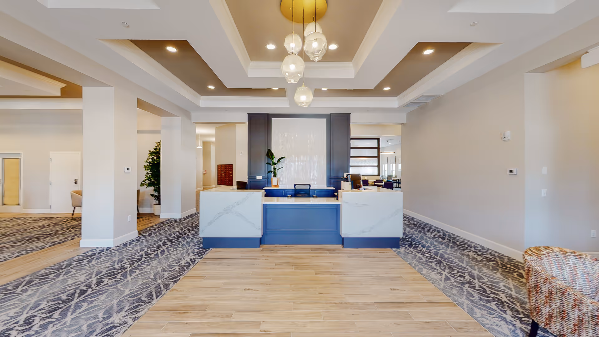 Bright modern reception lobby with a central desk, hanging pendant lights, and patterned carpeting.