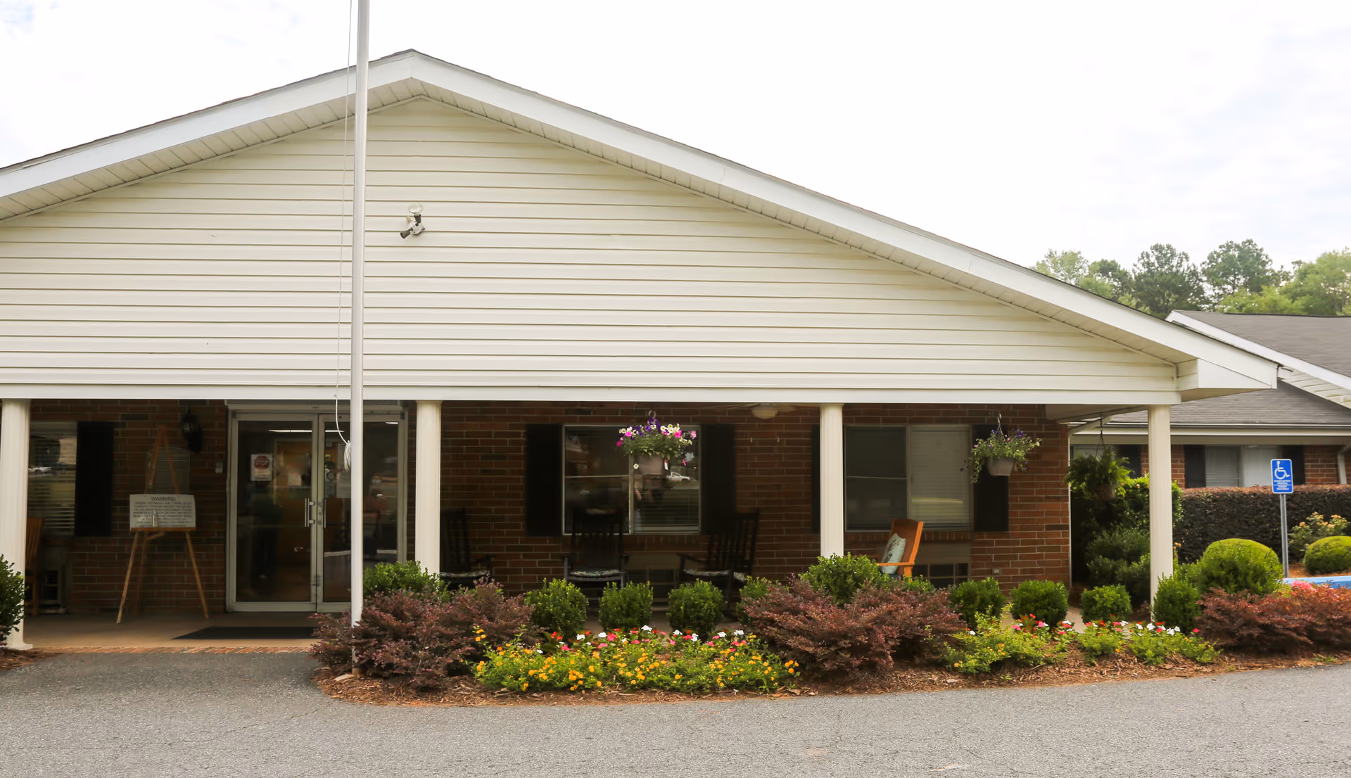 Front entrance of the Heritage Inn of Barnesville showing a covered porch with columns, hanging baskets, seating, and landscaped flower beds.