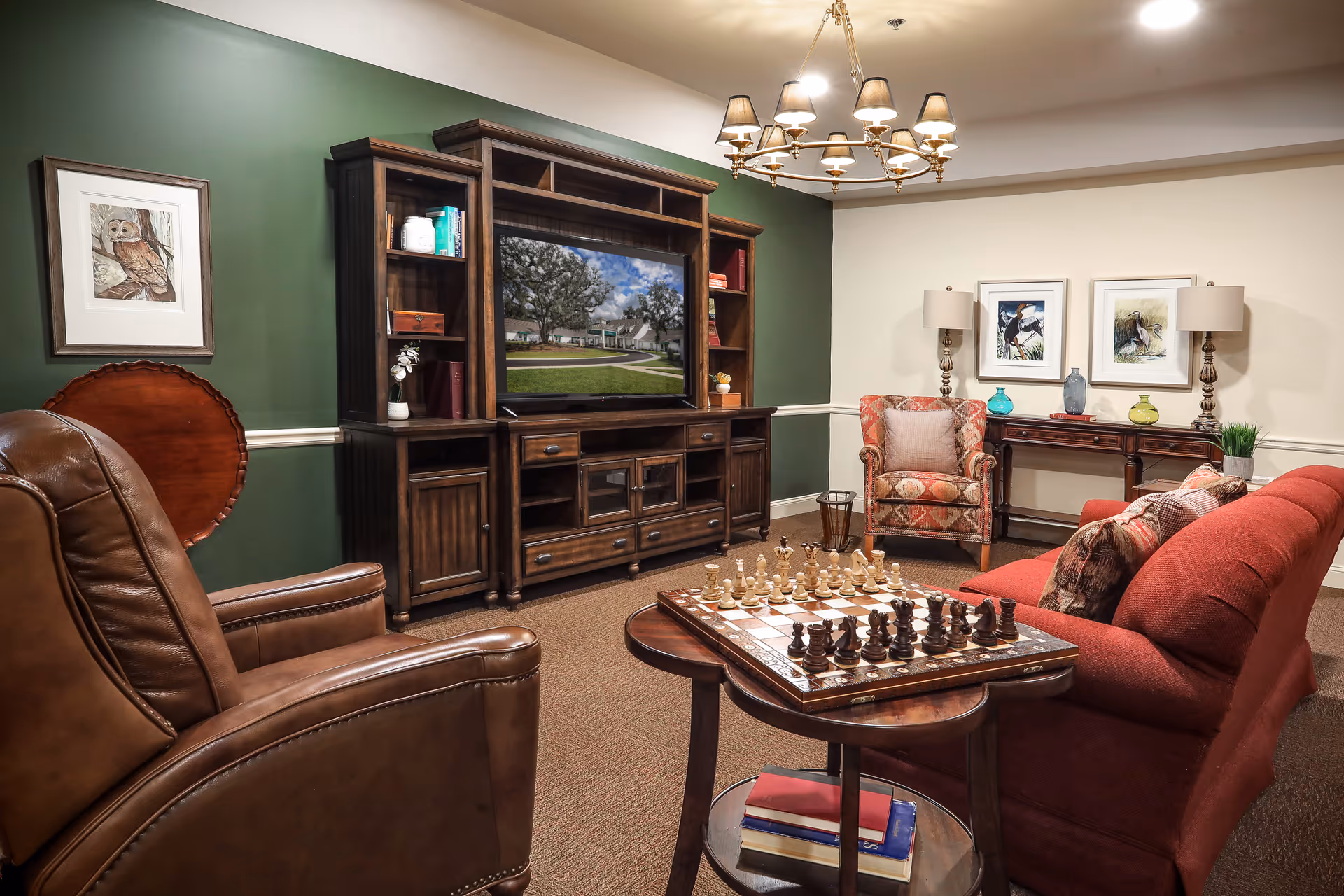Cozy living room with leather chairs, a red sofa, a wooden entertainment center with TV, and a chessboard on a small table.