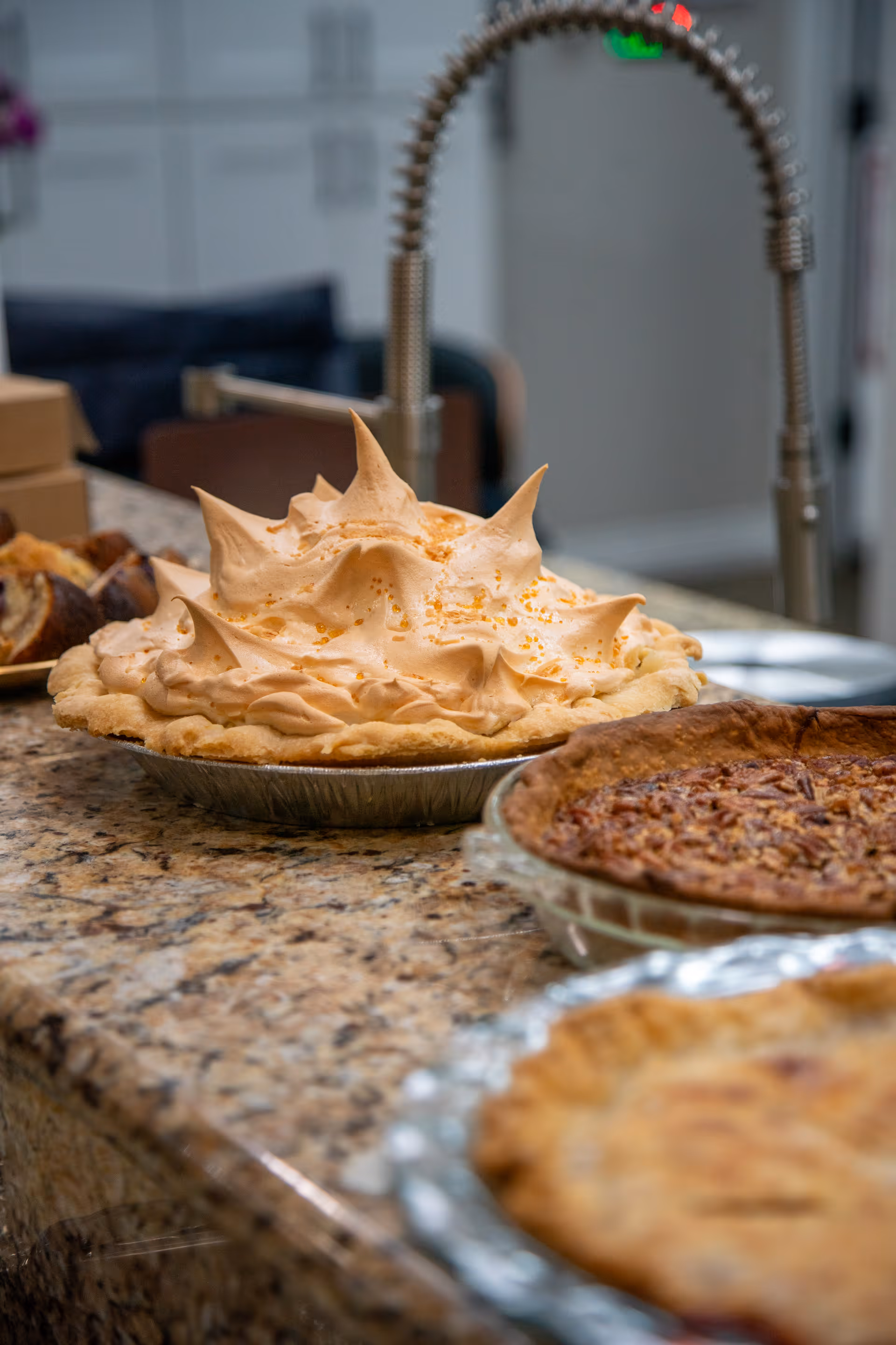Several freshly baked pies arranged on a granite kitchen countertop with a tall curved faucet in the background.
