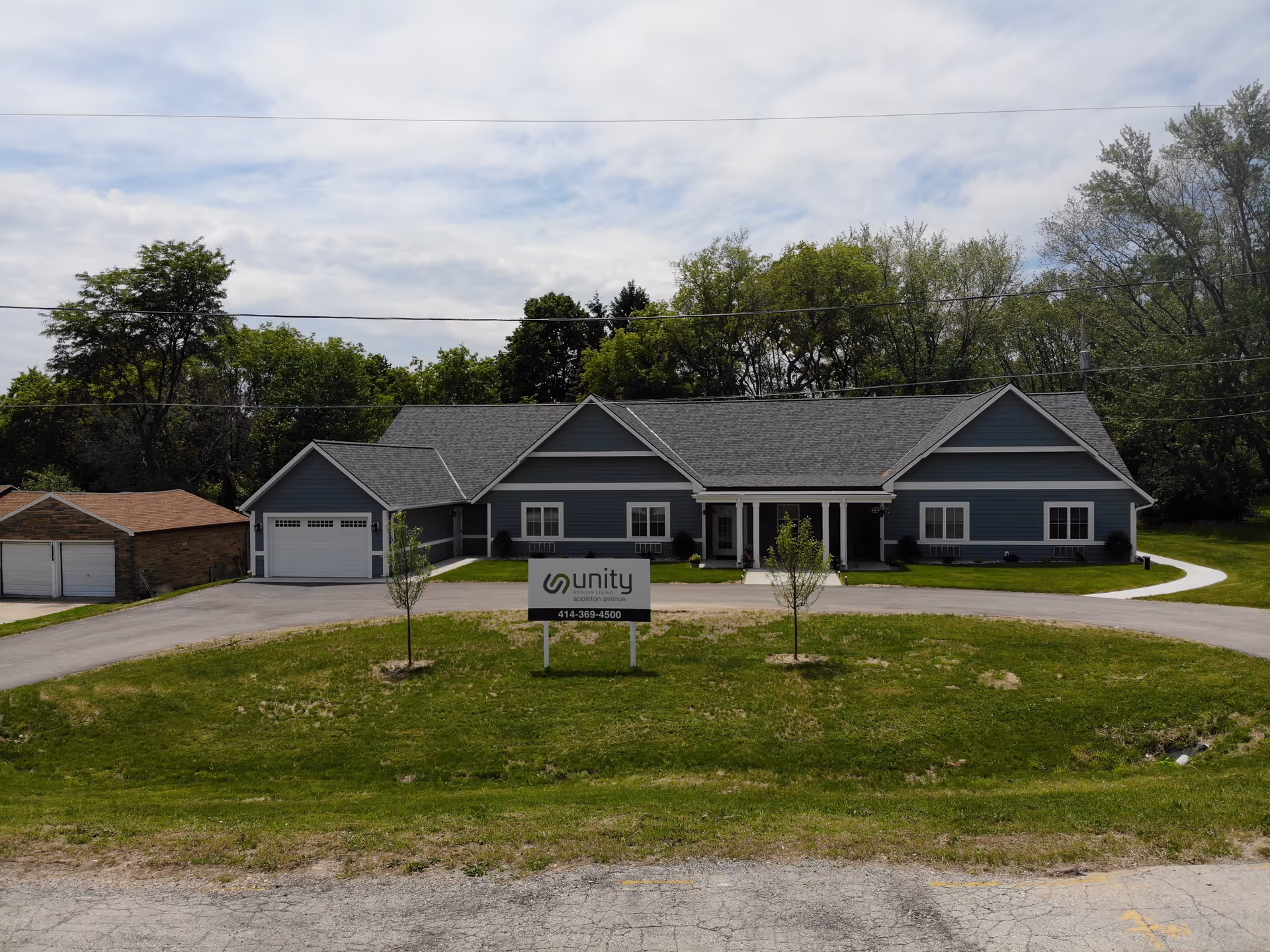 Single-story blue senior living building with a 'Unity' sign on the lawn and a circular driveway in front.