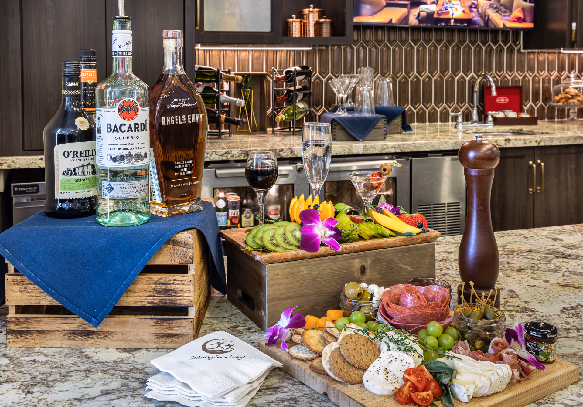 A marble kitchen/bar island topped with liquor bottles, wine glasses, and a large charcuterie and fruit display.