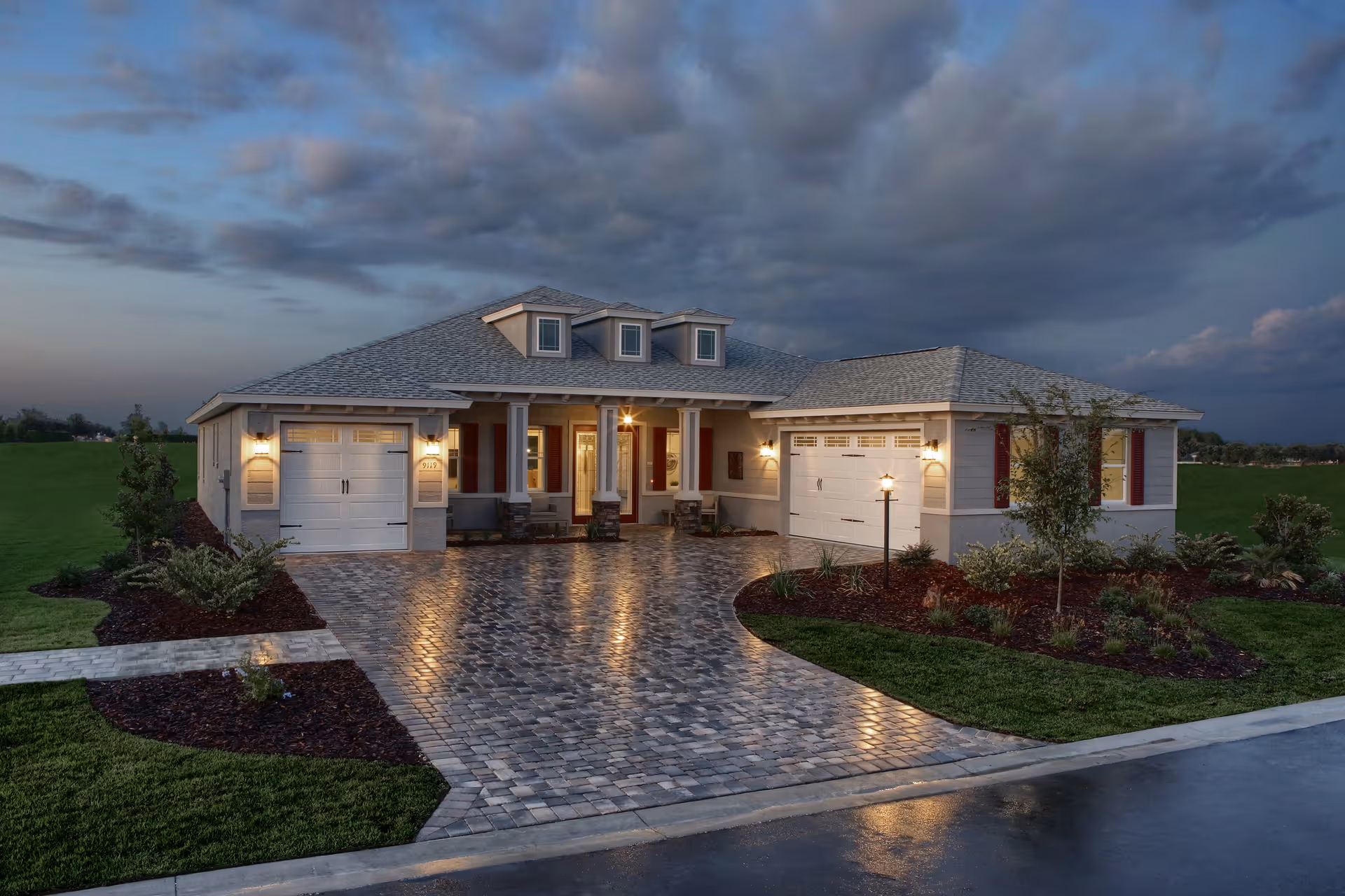Front view of a single-story house with illuminated porch lights and two garages at dusk.