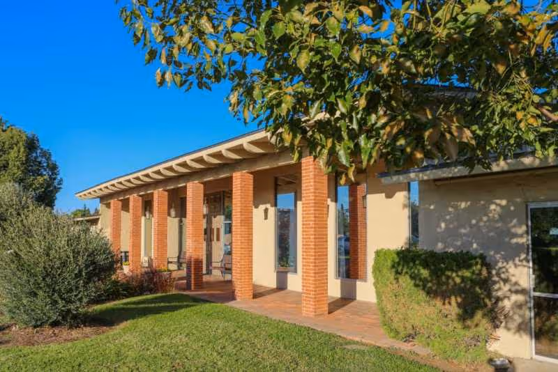Sunlit exterior of Magnolia Post Acute Care with brick columns and front entrance.