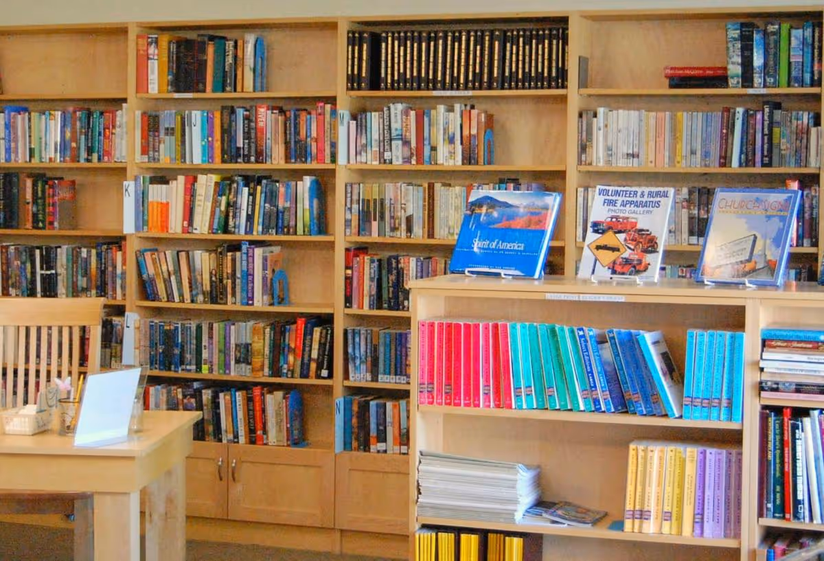 Wooden bookshelves filled with books and a small table in a cozy library room.
