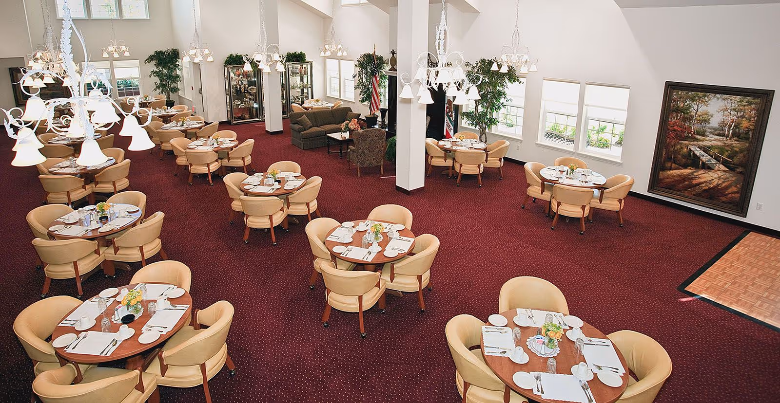 Spacious dining room with multiple round tables set for meals, chandeliers, and a small seating area.