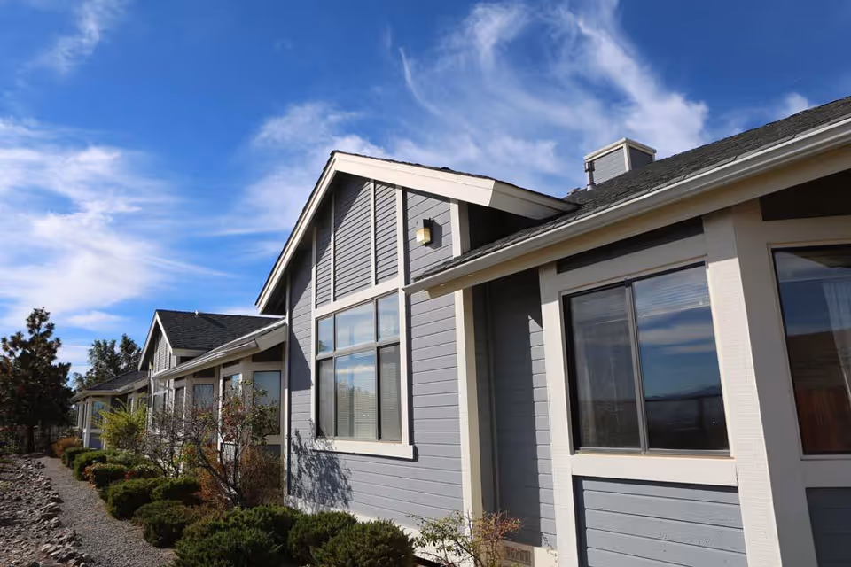 Single-story gray building with large windows and landscaping under a blue sky.