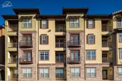 Exterior front of a multi-story Mediterranean-style apartment building with balconies and stone and stucco facades under a clear blue sky.