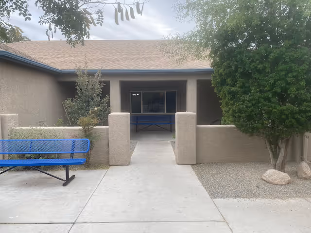 Exterior courtyard entrance of a single-story stucco building with a walkway and blue benches.