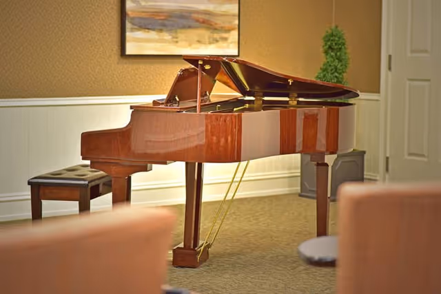 Polished grand piano in a lounge with a bench, framed art, and seating blurred in the foreground.