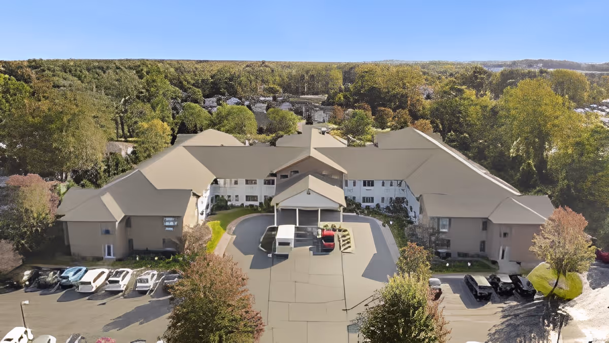 Aerial view of a large senior living facility with a covered entrance, parking lot, and trees surrounding the building.