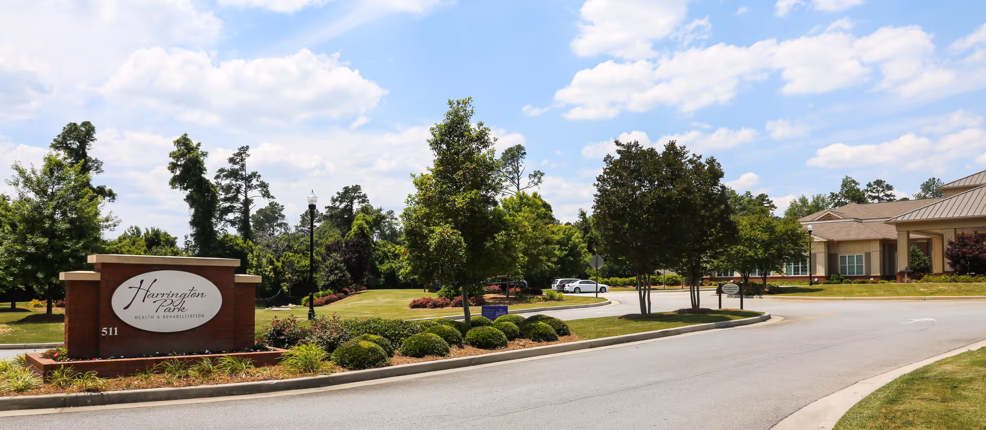 Front entrance driveway and landscaped grounds with a brick sign for Harrington Park Health & Rehabilitation and the facility building in the background.