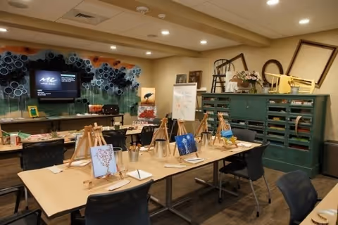A well-lit interior craft room with tables arranged with easels, canvases, and painting supplies for an art class.