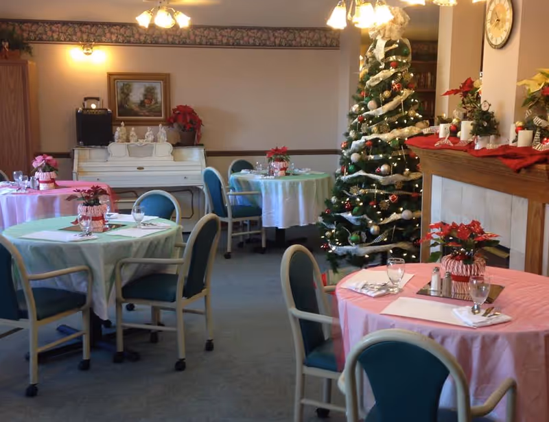 Festively decorated dining room with round tables set for meals, a Christmas tree, and a fireplace.