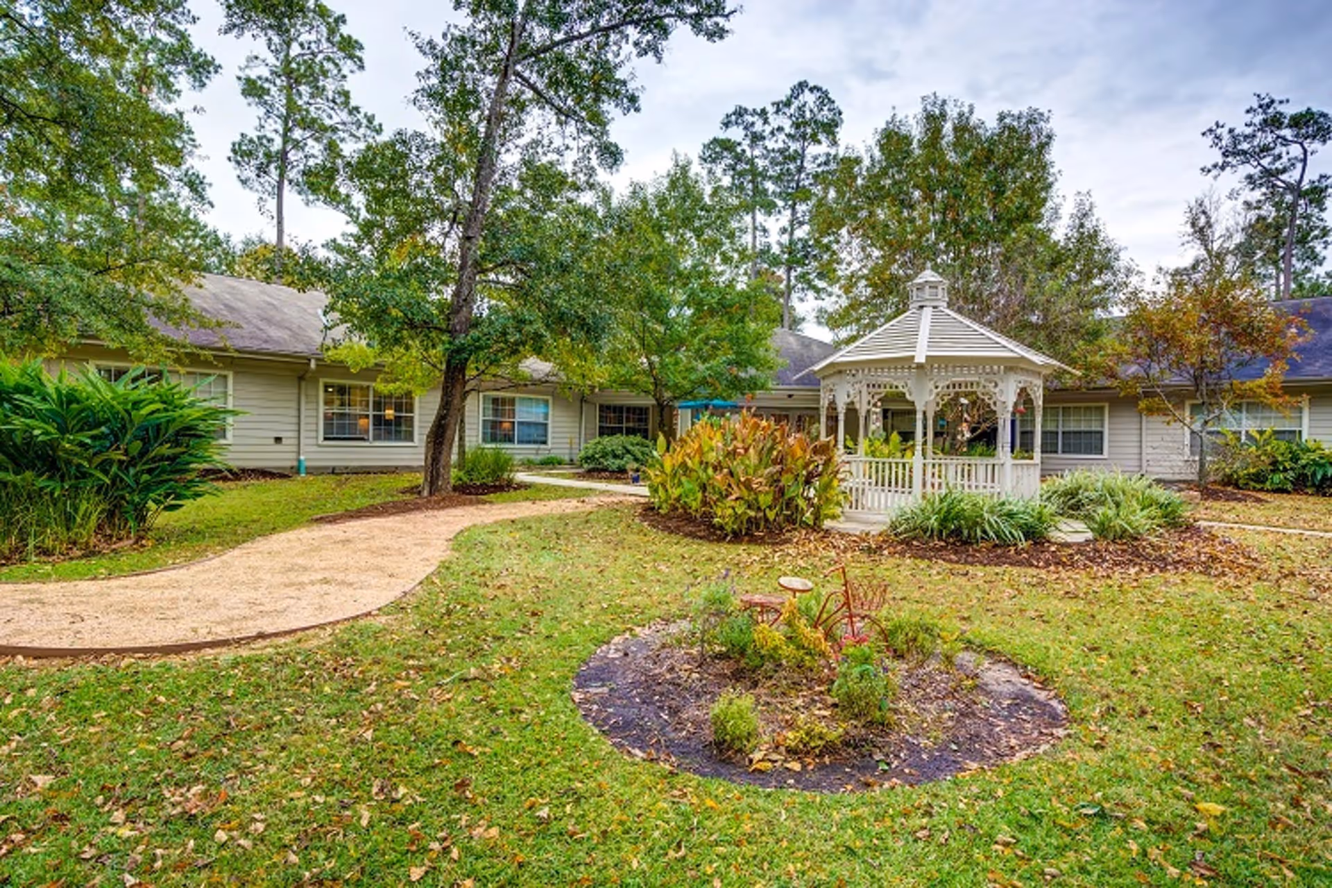 Grassy courtyard featuring a white gazebo, walking path, trees and a surrounding single-story building.