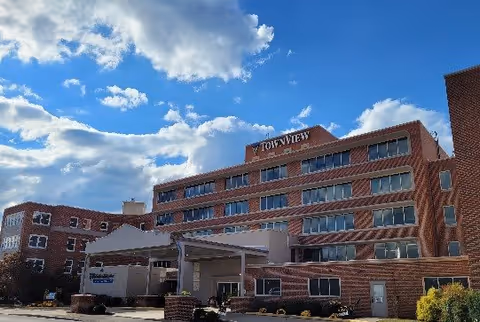 Front view of the multi-story TownView Senior Living brick building with a covered entrance under a partly cloudy blue sky.