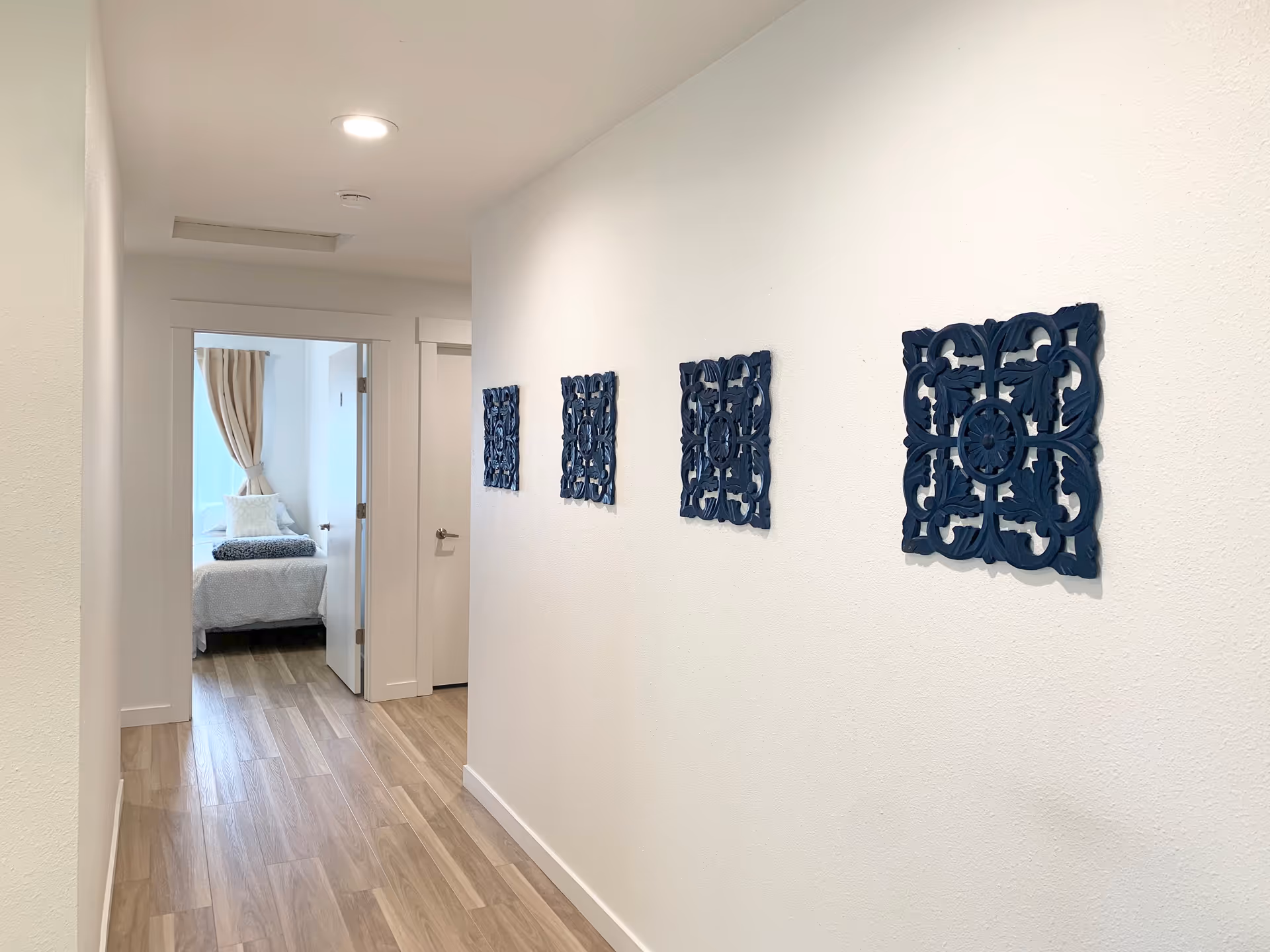 Bright interior hallway with wood-look flooring and four blue decorative wall panels leading to a bedroom.