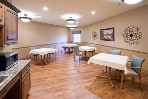 Interior dining room with several tables covered in white tablecloths and blue chairs.