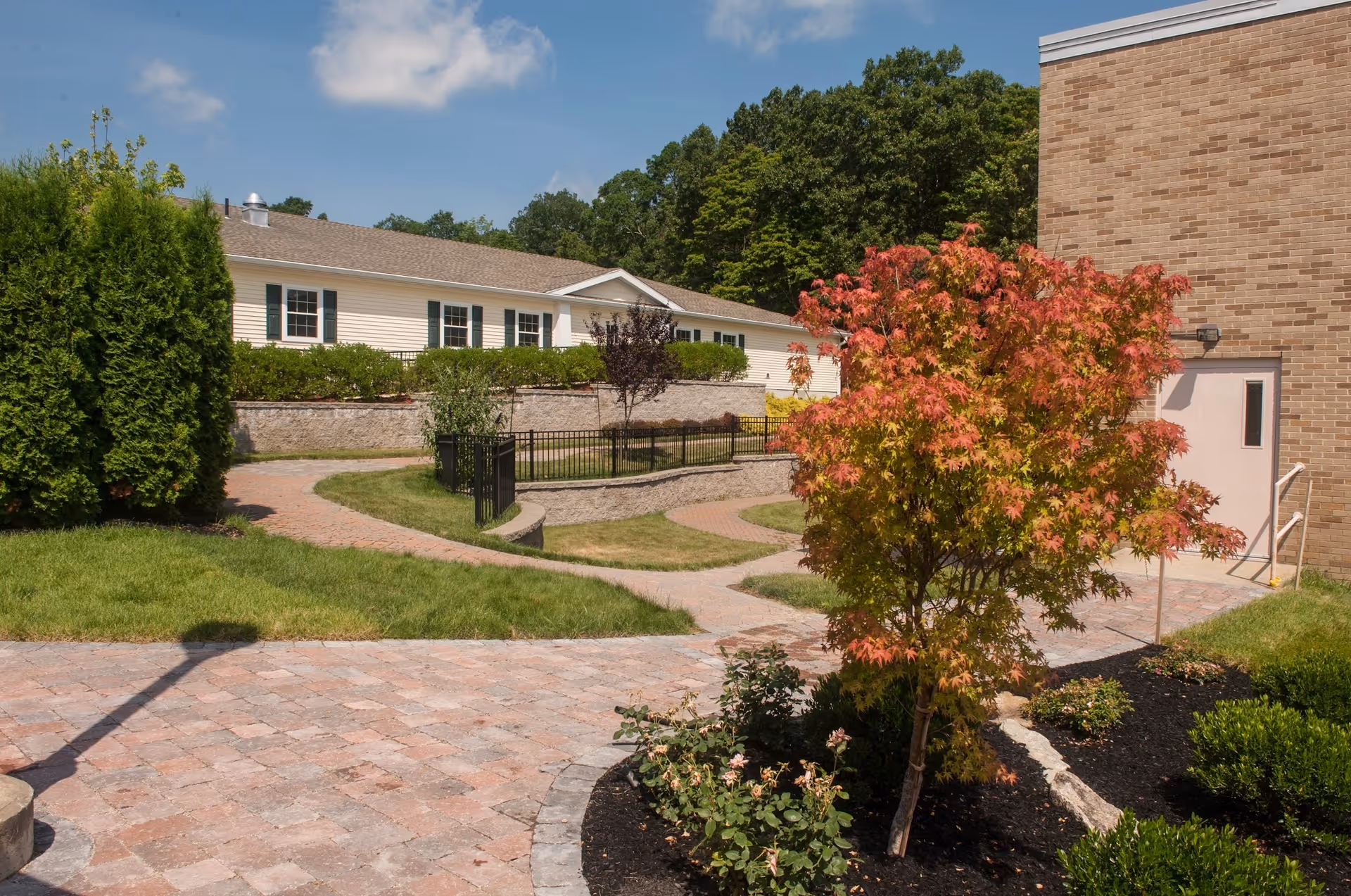 Landscaped outdoor courtyard with brick pathways, a small tree with orange leaves, and adjacent buildings.