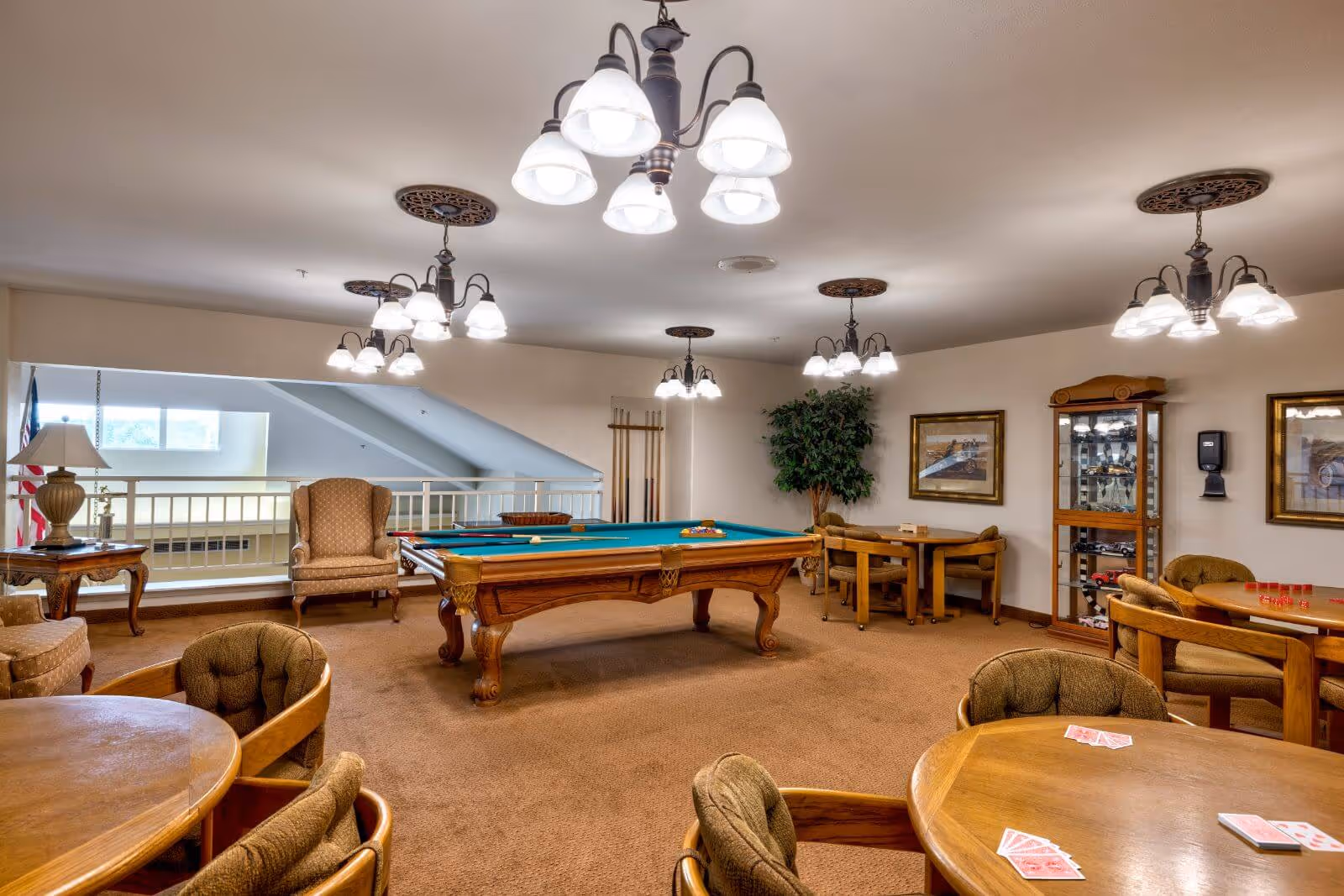 Community game room with a pool table, card tables, upholstered chairs, and multiple hanging light fixtures.